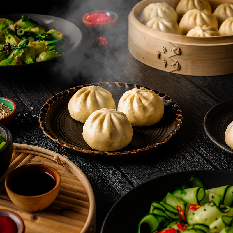 steamy bao in a small dish on a table surrounded by other food items