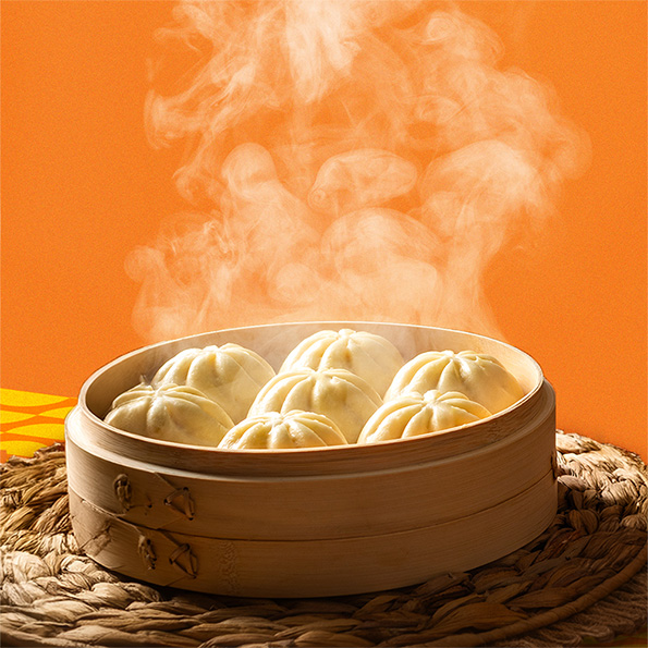 Steaming bao in a dumpling steamer basket on a weaved placemat with an orange backdrop