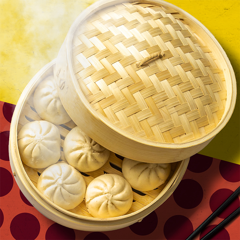 Steaming bao in a dumping steamer basket on a yellow and polkadot pattern table